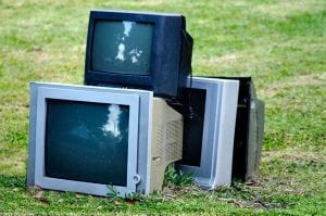 CRTs stacked on a grass lawn.