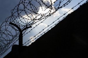 Dramatic clpuds behind a barbed wire fence prison wall.