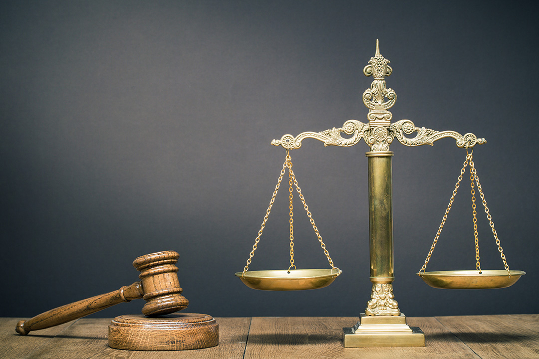Court scales and gavel on wooden desk with gray background.