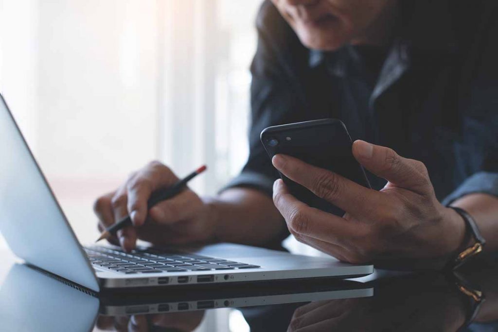 Person using a cell phone and laptop.