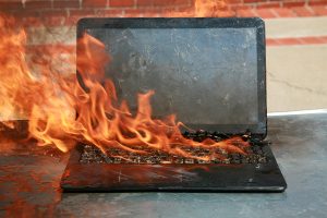 Burning laptop and keyboard, equipment fire due to faulty battery and wiring. Laptop Computer setting the world on fire. Laptop burning in flames. Fire hazard. Losing valuable data. Laptop Damage.