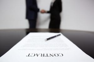 Contract with two people shaking hands in the background.