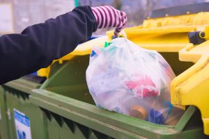 A person drops a bag of mixed plastics into a collection bin.
