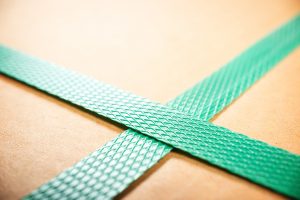 Close-up of green plastic strapping around a cardboard box.