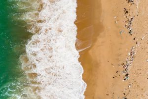 View from above a wave coming ashore with debris on beach.