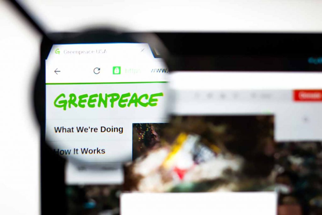 Greenpeace website logo on screen under magnifying glass.
