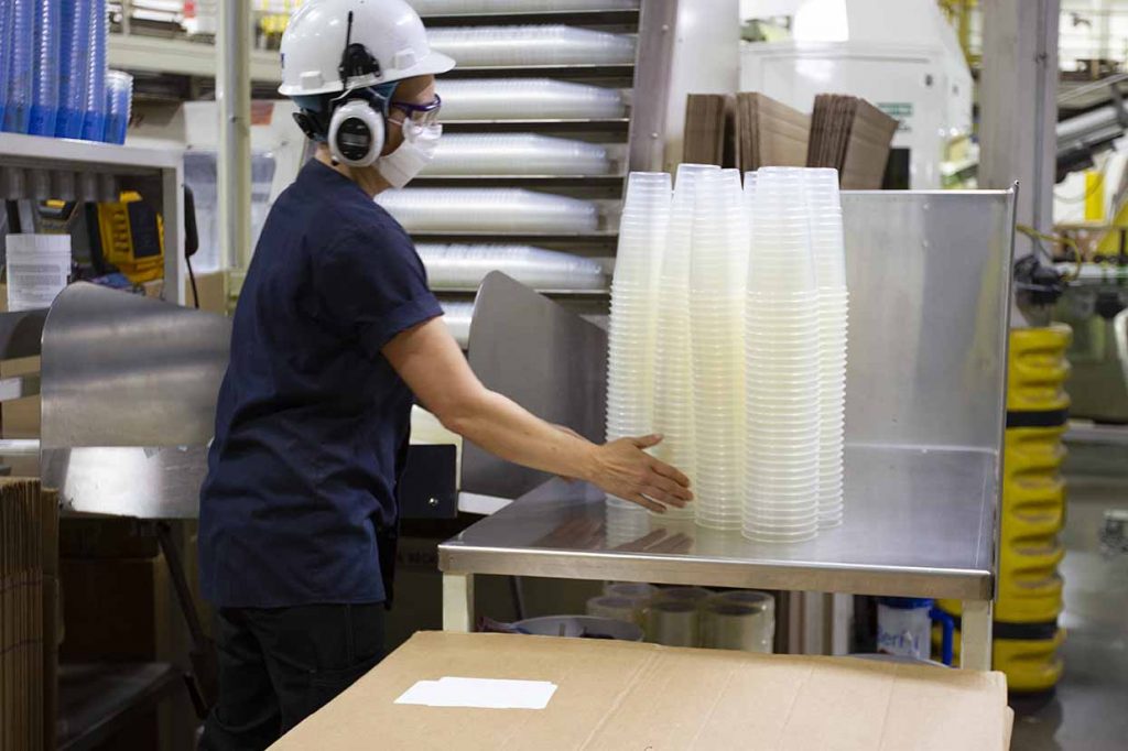Employee at factory with Berry PP cups containing chemically recycled plastic.
