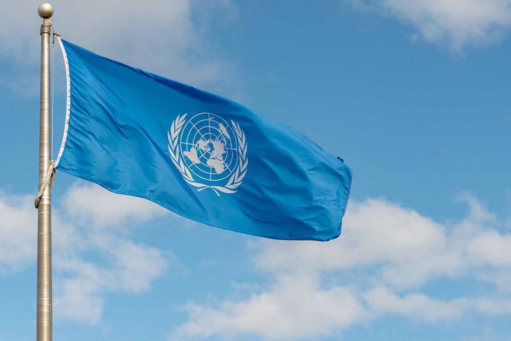 United Nations flag flying against blue sky and clouds.