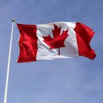 Canadian flag against blue sky background.