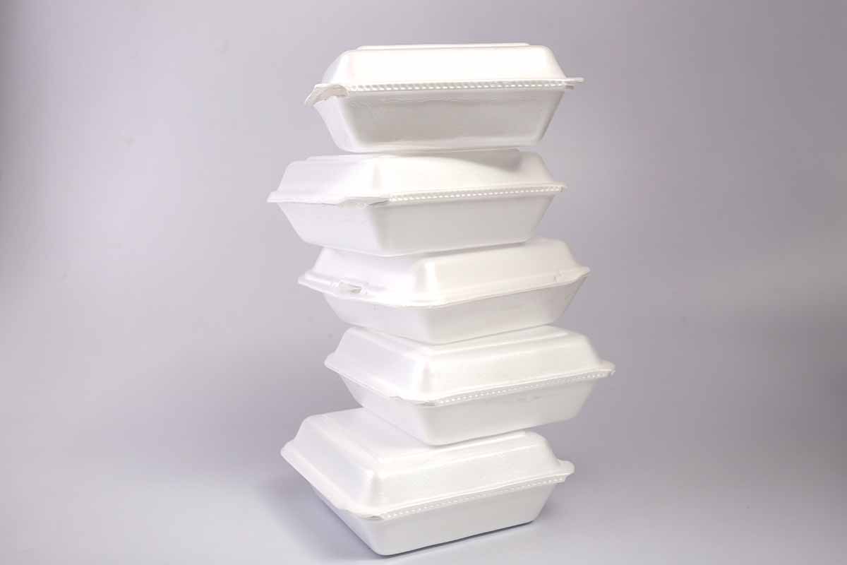Foam PS to-go food containers stacked against a grey background.