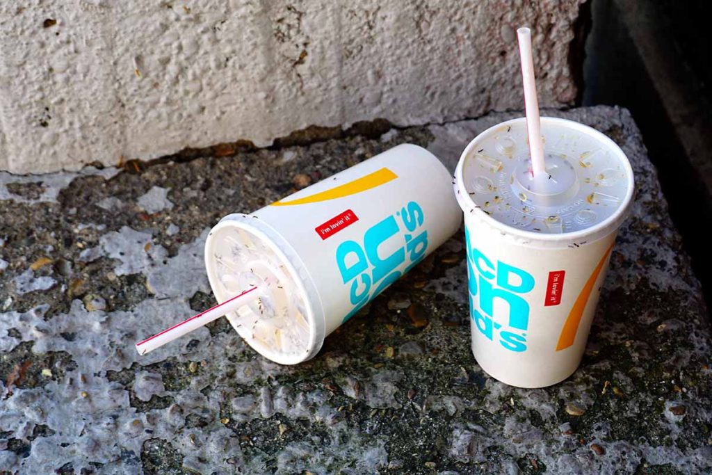 McDonald's drink cups and straws discarded on concrete.