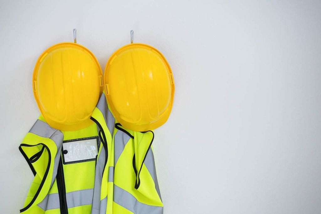 Safety vests and hard hats hanging on a wall.