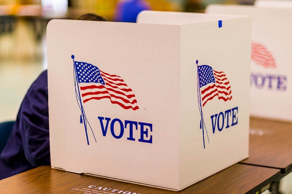 A person sitting at a tabletop voting booth.