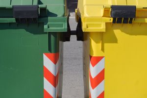 Green and yellow recycling and waste bins on a street.