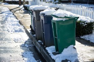Curbside recycling and trash carts on a snowy street.