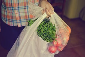 Person carrying vegetables in plastic bags.