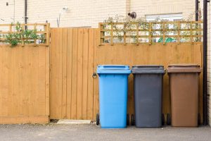 Curbside collection bins against a wood fence.