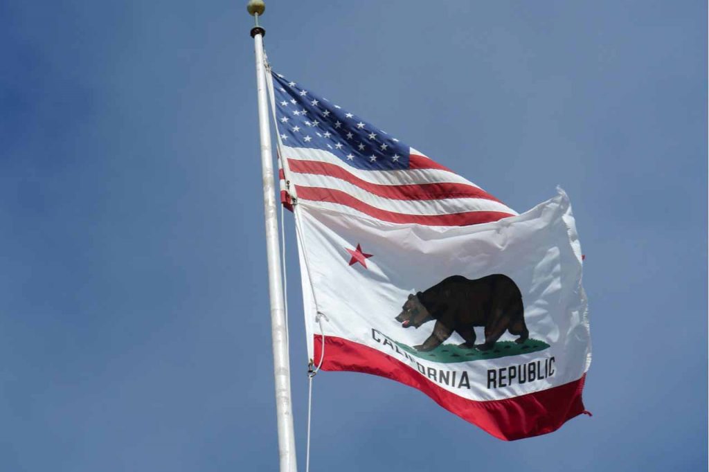 U.S. and California flags against a blue sky.