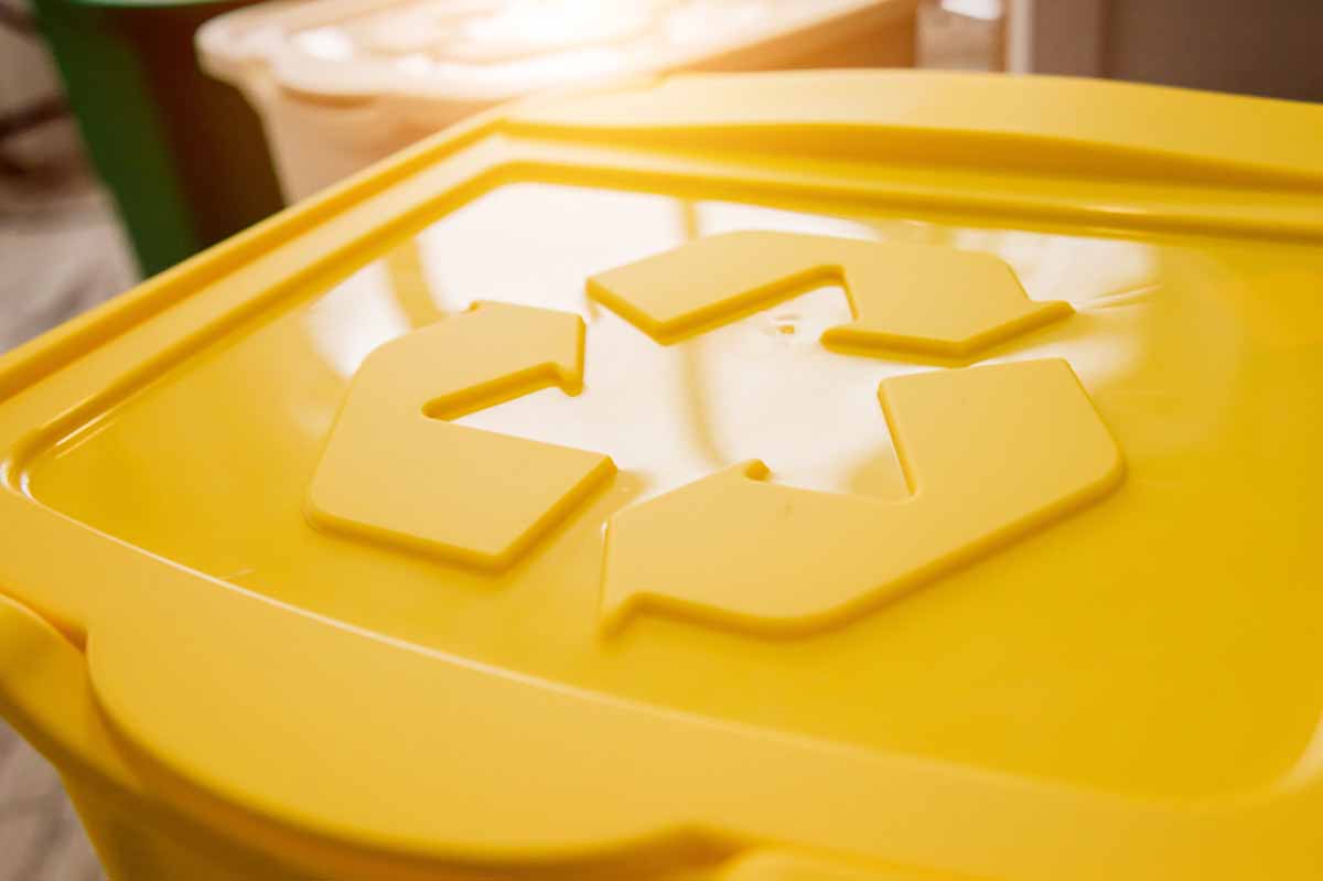 Yellow recycling collection container with chasing arrows symbol.