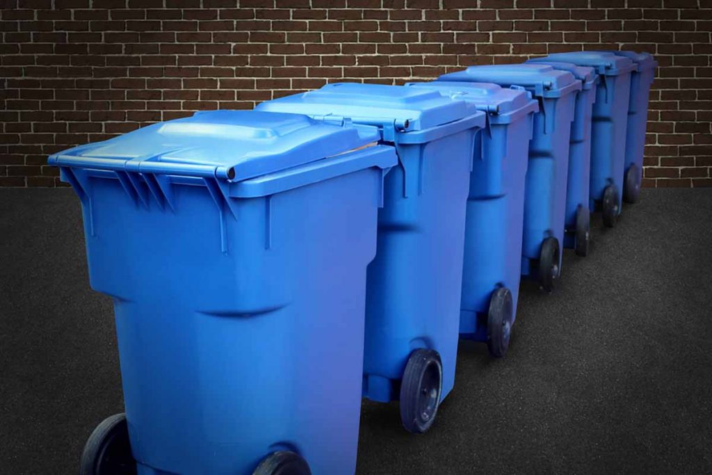 Blue recycling bins lined up against a brick background.