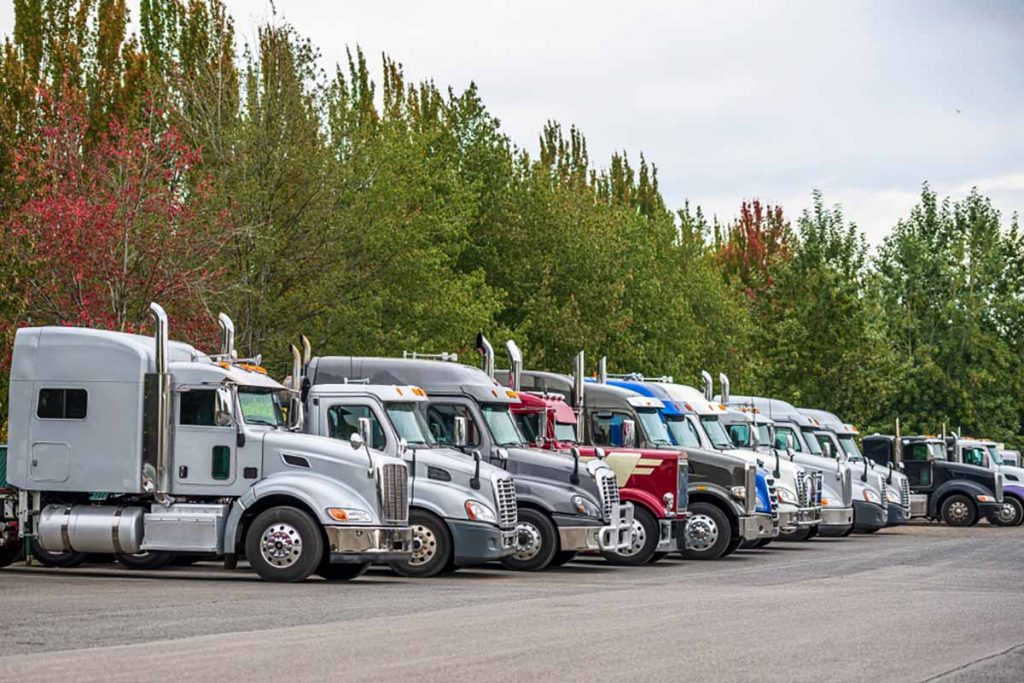 Many hauling trucks parked in a lot.