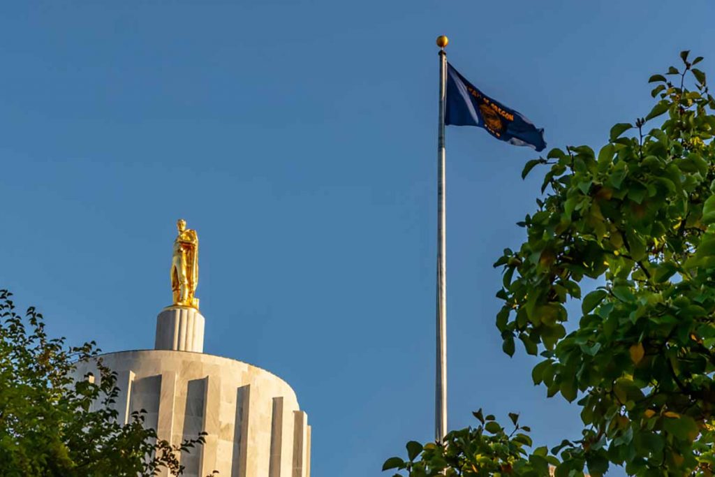 Oregon state capitol building with state flag and blue sky.