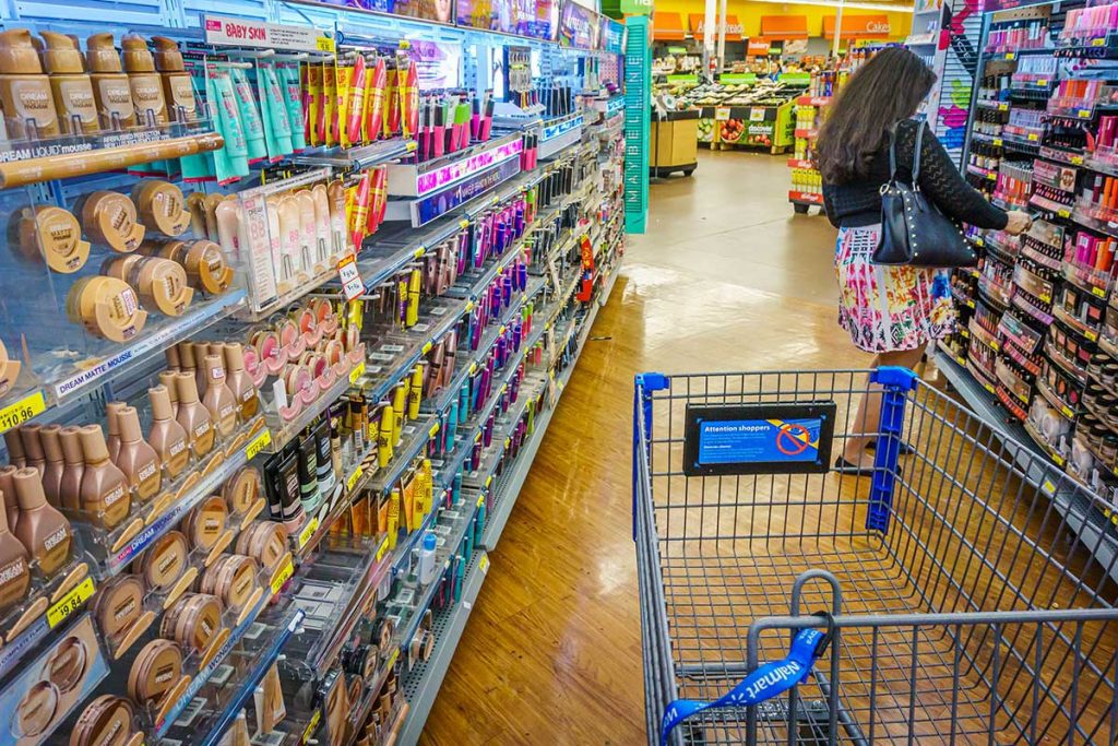 Walmart beauty products aisle with cart and shopper.