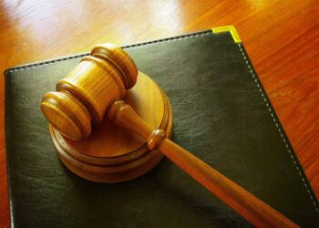 Court gavel rests on a leather binder on a desk.