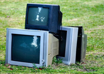 CRTs stacked on a grass lawn.