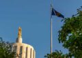 Oregon state capitol building with state flag and blue sky.