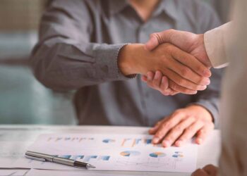 Business handshake with documents on desk.