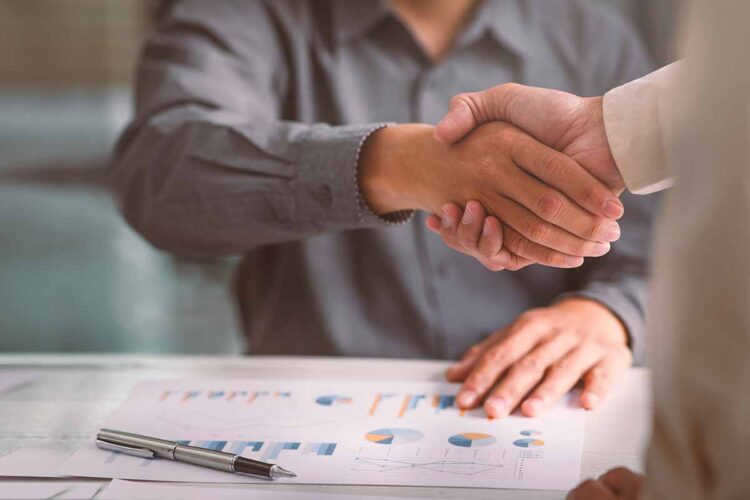 Business handshake with documents on desk.