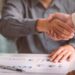 Business handshake with documents on desk.