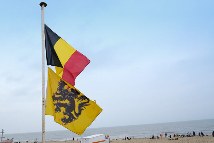 Belgian and Flemish flags fly against a backdrop of an ocean beach